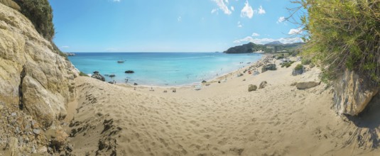 A quiet place on Tsambika sandy beach of Tsambika with clear blue sea and rocks under a sunny sky,