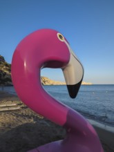 Pink flamingo pedal boat on Tsambika sandy beach with sea in the background at sunset, Tsambika