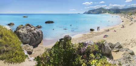 Picturesque Tsambika bay with clear water, rocks and sandy beach. People enjoying the sun, a boat