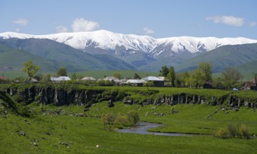A village in a green landscape with snow-capped mountains in the background, Saratovka, Lesser