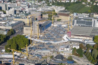 Panoramic view of modern construction site with glass structures and cranes in an urban green area,