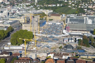 Modern construction site with glass roofs and cranes in an urban environment, surrounded by trees,