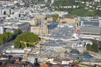 Urban construction project with glass structures and cranes, embedded in a green urban backdrop,