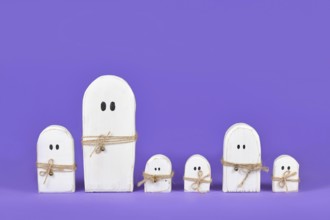 Cute wooden white Halloween ghost ornaments in a row on purple background
