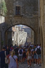 A busy historic alleyway with people walking through an alley under a stone arch, Knights Street,
