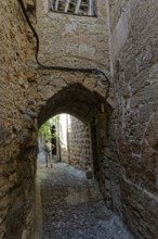 Cobbled alley with arched passageway and stone walls, a man in the background, Medieval town of