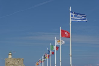 Several flags waving in the wind against a clear blue sky, including the Greek flag, Mandraki
