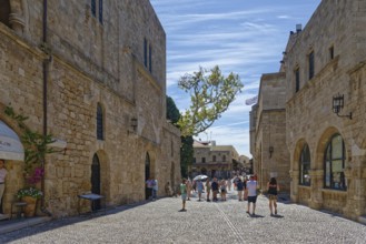 Historic old town street with cobblestones and old buildings under a blue sky full of tourists,
