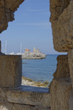 View through a wall of a medieval fort of Saint Nikolaos by the sea with sailing boats, Mandraki