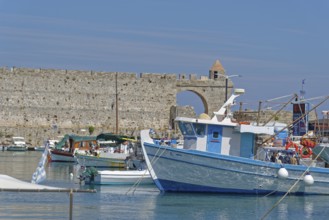 Fishing boats lying in the calm water in front of a historic city wall, Mandraki harbour, Medieval