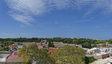 View of a historic old town with many trees and traditional buildings under a clear blue sky,