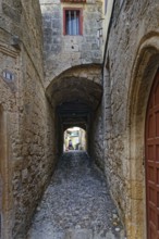 Narrow stone-paved alley with arches and high stone walls, quiet atmosphere, Medieval Town of