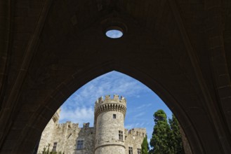 View through a stone arch to a medieval castle with tower under a blue sky, Grand Master's Palace,