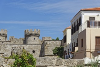 Castle with medieval stone towers next to a Mediterranean building under a blue sky, Grand Master's