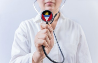 Female doctor holding stethoscope with Antigua and Barbuda flag. National health system of Antigua
