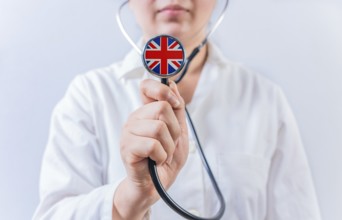 Female doctor holding stethoscope with United Kingdom flag. National health system of United