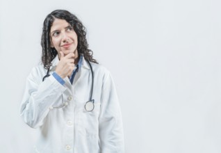 Young female doctor thinking with her hand on her chin, isolated. Thoughtful young female doctor
