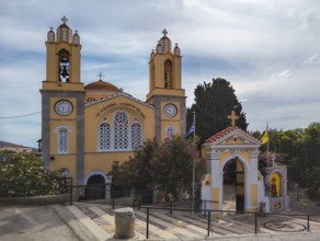 Yellow church with bell towers and flowers under a blue sky, Greek Orthodox Church of Saint