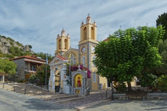 A yellow church with towers and bells surrounded by trees under a cloudy sky, Saint Pantaleon Greek