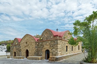 Small stone church Kimisis tis Theotokou with red roofs, surrounded by trees under a clear blue