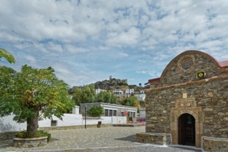 Small church Kimisis tis Theotokou made of stone with red roofs, blue sky and the castle ruins
