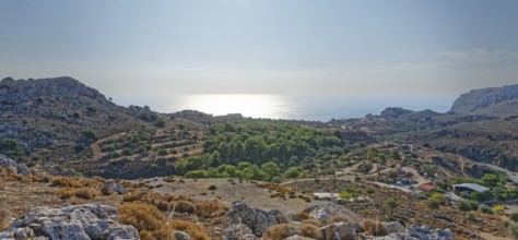 View over a barren range of hills near Stegna to the sea under the morning sun, Stegna,