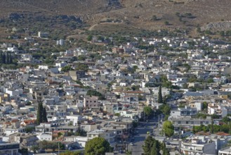 Town of Archangelos with densely built blocks of houses and green trees on hilly terrain,