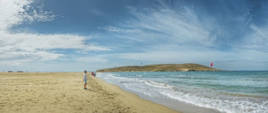 Wide sandy beach of Prasonisi with gentle waves, distant peninsula and kite surfers under a blue