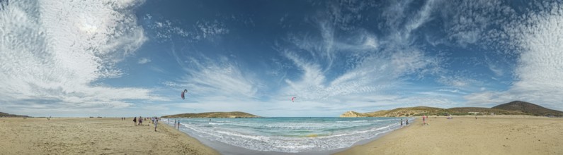 Beach panorama of Prasonisi with light sand, blue sea and two kite surfers under a cloudy sky,