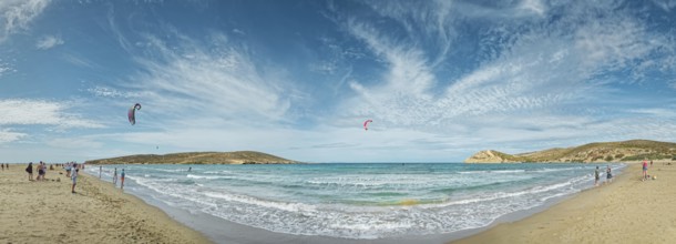 Spacious beach of Prasonisi with light sand, blue sea and two kite surfers under a cloudy sky,