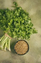 A bundle of fresh cilantro sits neatly tied, next to a small bowl filled with coriander seeds. The