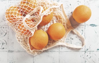 Oranges in a mesh bag, on a textured surface, sunlight, no people