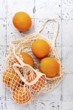 Oranges in a mesh bag, on a textured surface, sunlight, no people