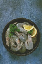 Fresh raw white-footed shrimp, tiger prawns vannamey, on a clay plate, with lemon and herbs, on a