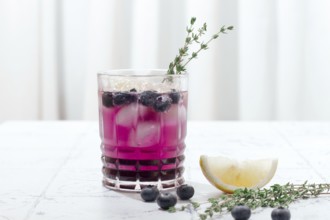 Refreshing blueberry and thyme drink served with lemon in a clear glass on a light surface