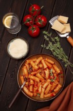 Rigatoni pasta with meat sauce and parmesan cheese on a dark wood table with ingredients, top view