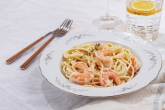 Pasta with shrimp and thyme, served on a white plate, with a glass of white wine, the table is set,