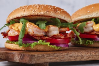 Two shrimp burgers and buns with sesame seeds, bacon, lettuce, tomatoes and onions, On a wooden