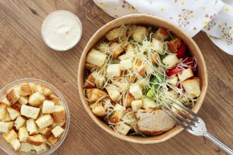 Caesar salad in a paper container, take it on the way, with sauce and croutons, on the table,