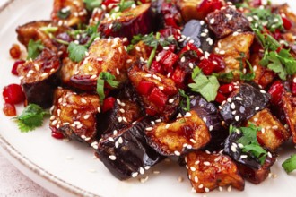 Fried eggplant, Chinese style, in sweet and sour sauce, with pepper and sesame seeds. on a white