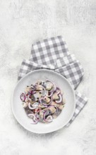 Salted herring, with spices and red onion, sliced fillet, on a plate, top view