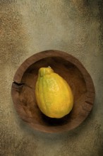 A vibrant yellow papaya is positioned in a rustic wooden bowl, resting on a textured surface that