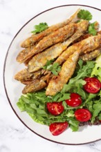 Fried crispy mullet fish, with fresh salad, on a plate with lime, no people