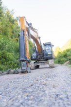An excavator on a gravel road, surrounded by green bushes, Hermann Hessebahn construction site,