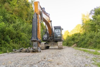A large excavator stands on a dirt road in a wooded area, Hermann Hessebahn construction site,