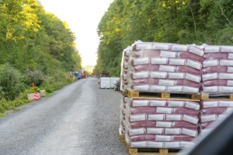 Stacked pallets of building materials line a gravel road in the forest, Hermann Hessebahn