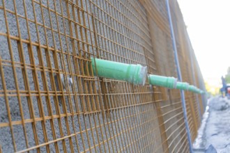 Metal grid with green pipes in front of a concrete wall on a construction site, Hermann Hessebahn