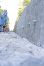 Large concrete wall and blue excavator on a gravel road, Hermann Hessebahn construction site, Calw,