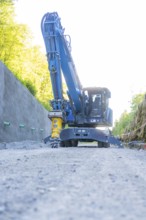 Blue excavator with hydraulic hammer on a path on a concrete wall, Hermann Hessebahn construction
