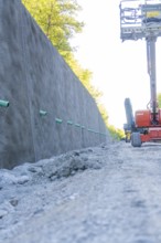 Concrete wall along a road with exposed earth and equipment on a construction site, Hermann